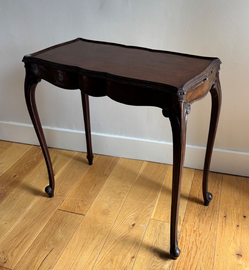 An Edwardian mahogany occasional table with a serpentine top, carved frieze, and slender cabriole legs. View II