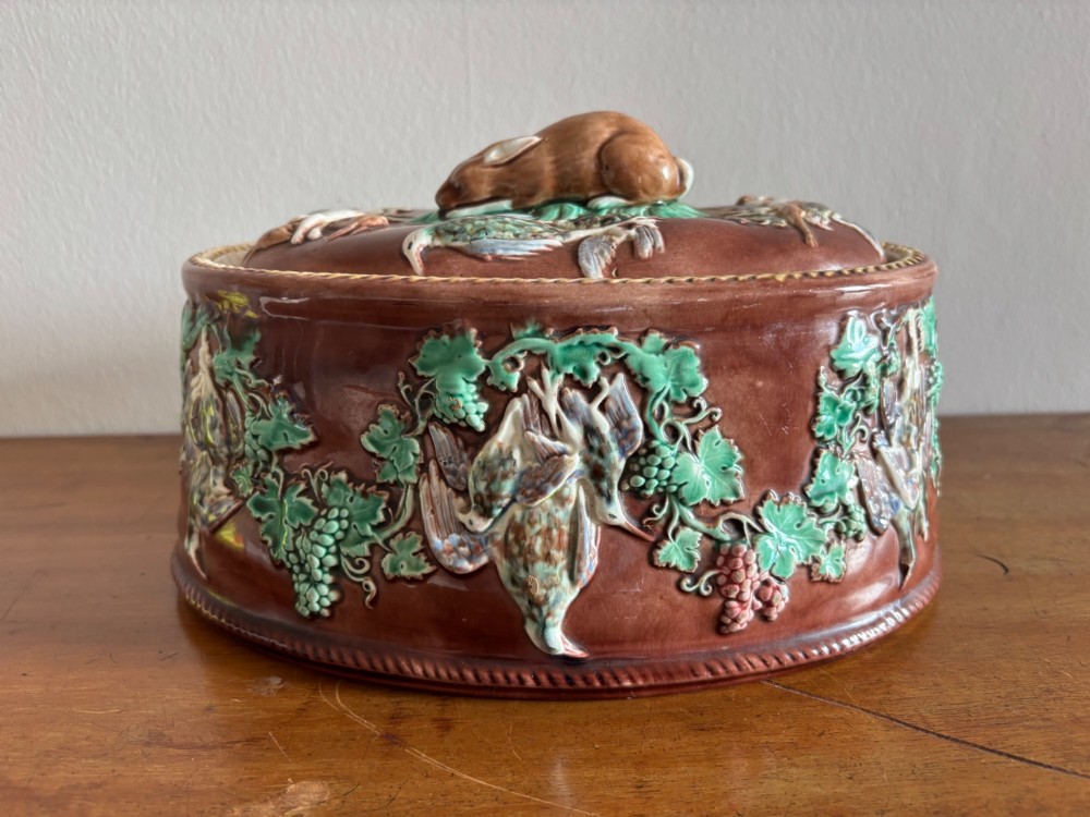 An oval brown glazed Victorian Wedgwood game pie dish decorated with green relief grapevines, hanging game birds, and a resting hare finial on the lid.
