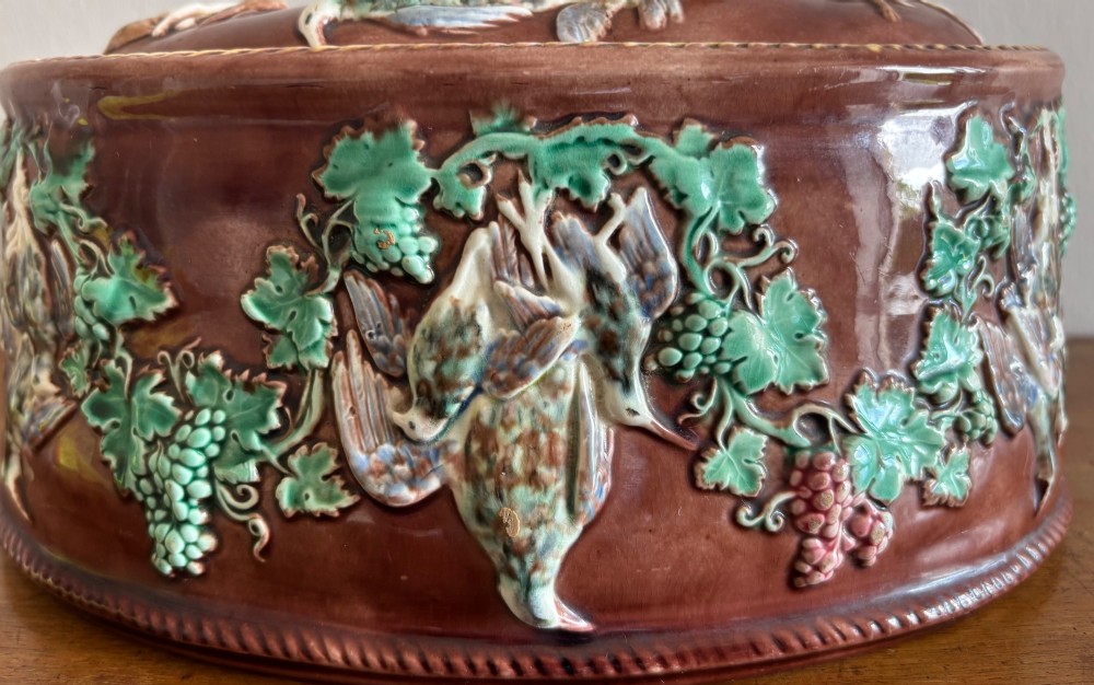 An oval brown glazed Victorian Wedgwood game pie dish decorated with green relief grapevines, hanging game birds, and a resting hare finial on the lid. View III