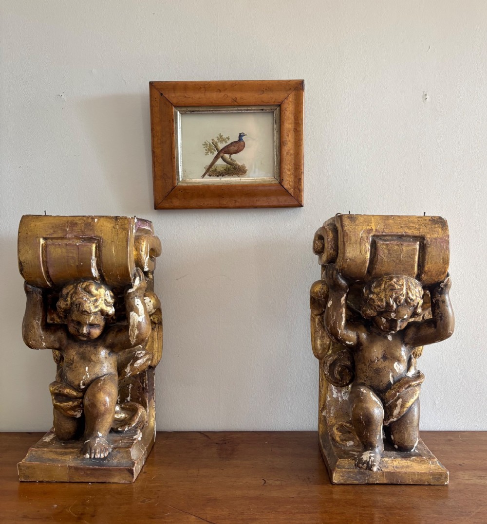 A pair of 19th-century carved giltwood wall brackets featuring winged cherub figures supporting scrolled capitals.