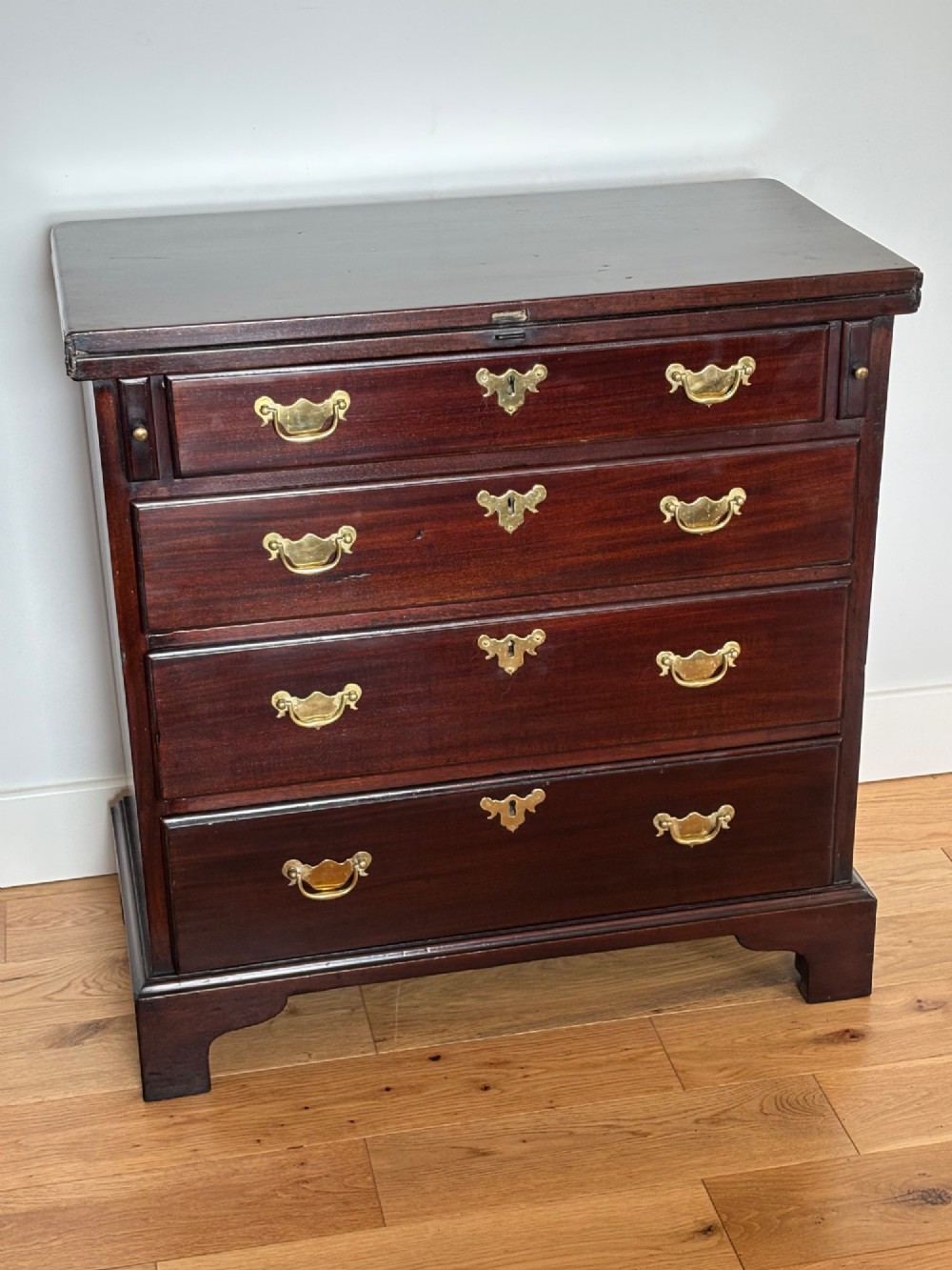 A George III mahogany bachelors chest featuring four graduated drawers with brass handles, a folding top, and bracket feet. View II