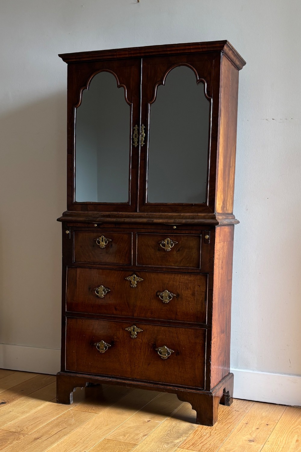 An eighteenth-century George II walnut cabinet on chest featuring arched door panels above drawers with brass handles and bracket feet.