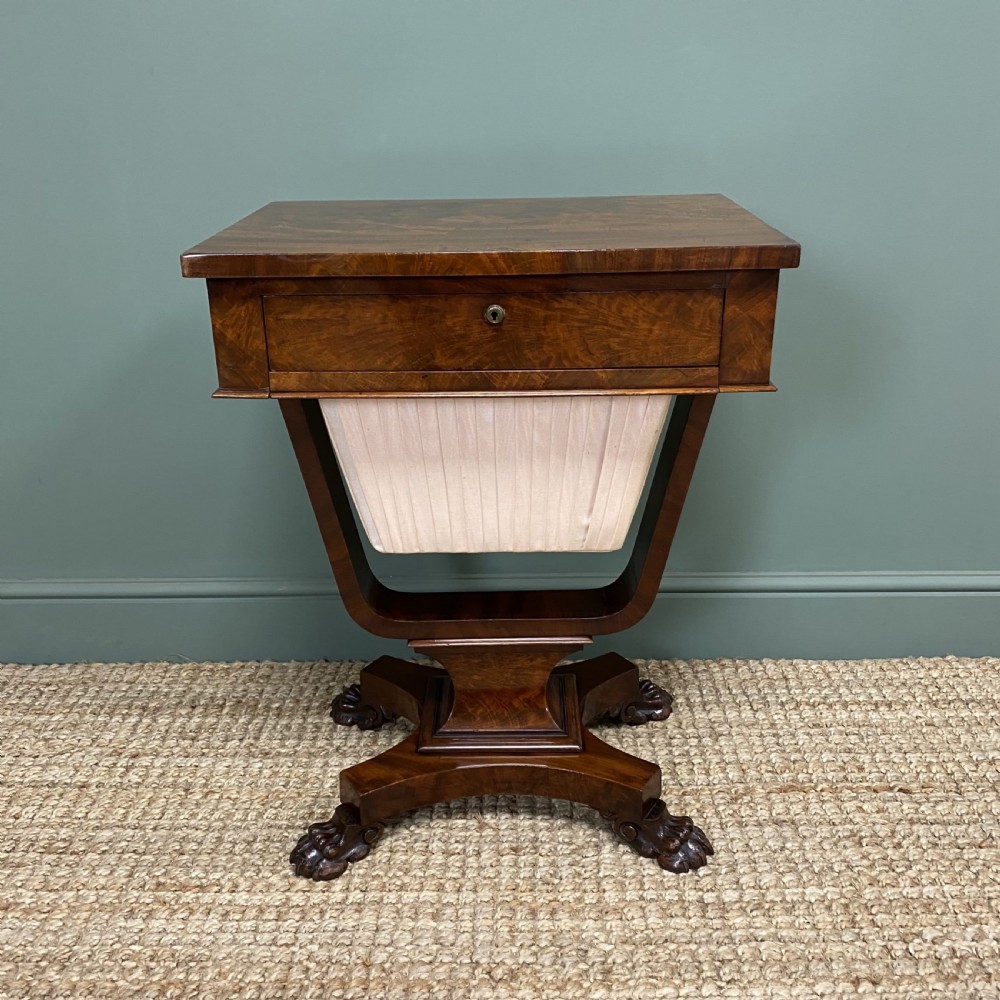 A William IV flame mahogany work table featuring a top drawer, pleated fabric work basket, U-shaped pedestal support, and carved claw feet.