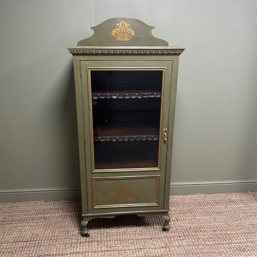 A muted green Edwardian display cabinet featuring a shaped pediment with gilt ornamentation, a single glazed door, and cabriole legs. View II