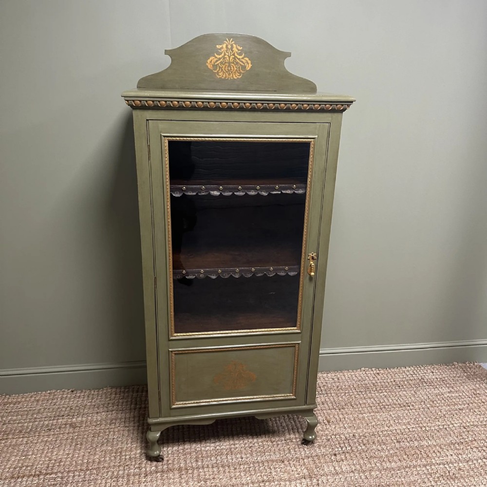 A muted green Edwardian display cabinet featuring a shaped pediment with gilt ornamentation, a single glazed door, and cabriole legs. View III
