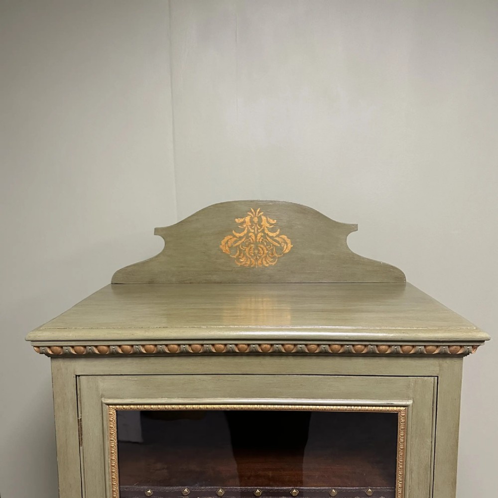 A muted green Edwardian display cabinet featuring a shaped pediment with gilt ornamentation, a single glazed door, and cabriole legs. View VII