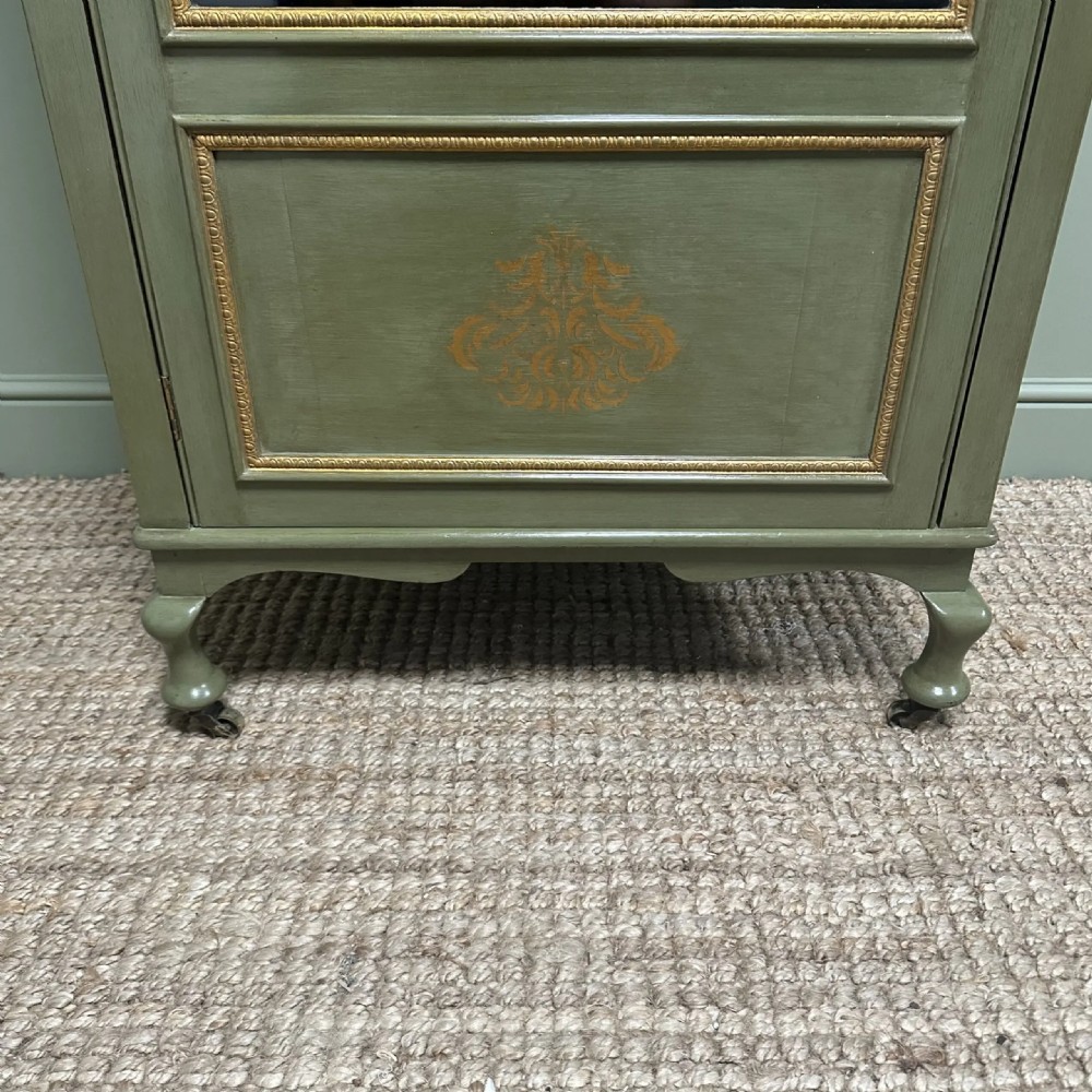 A muted green Edwardian display cabinet featuring a shaped pediment with gilt ornamentation, a single glazed door, and cabriole legs. View IX