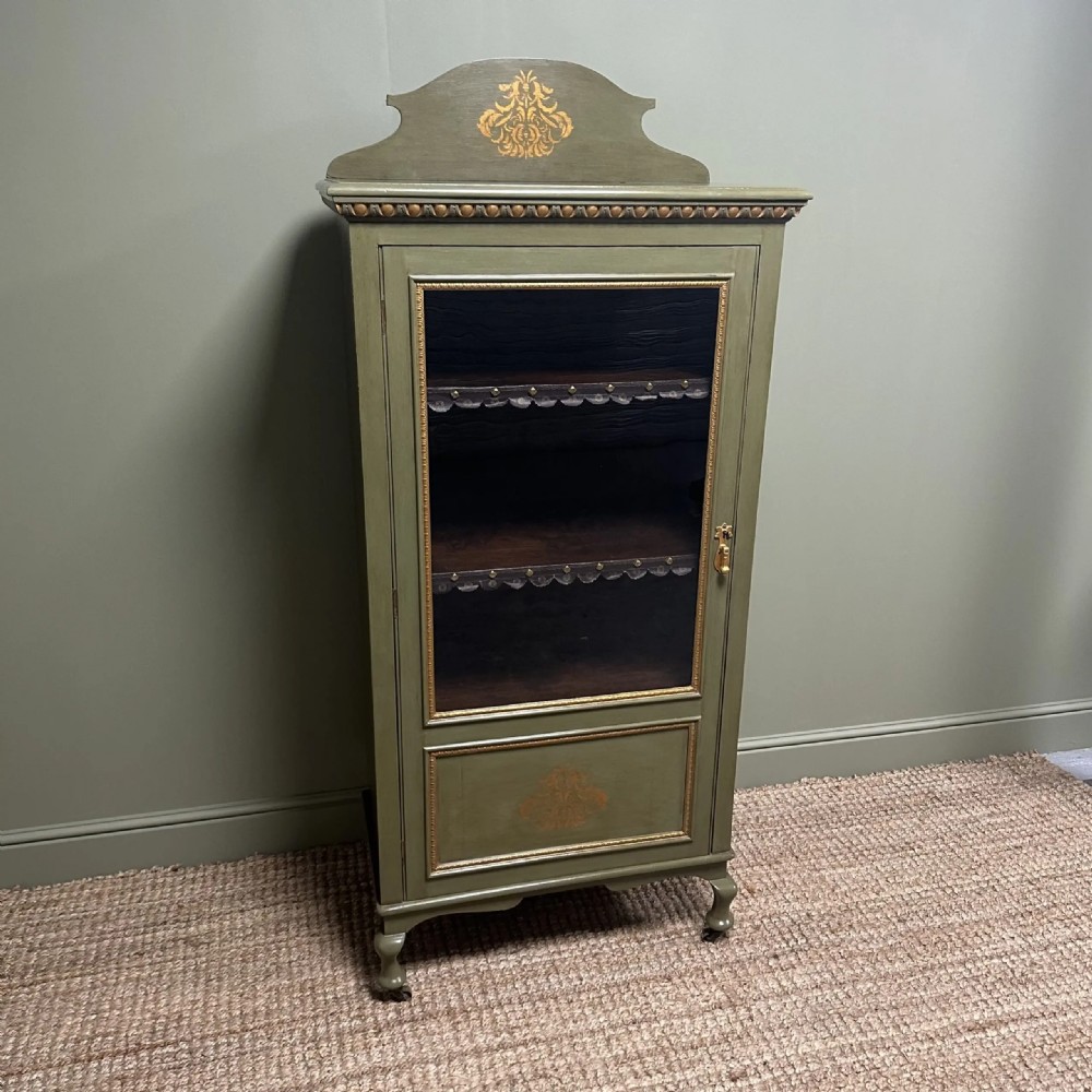 A muted green Edwardian display cabinet featuring a shaped pediment with gilt ornamentation, a single glazed door, and cabriole legs. View XI