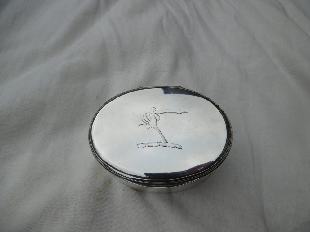 An 18th-century oval sterling silver box featuring a hinged lid engraved with a family crest depicting an arm holding a scimitar.