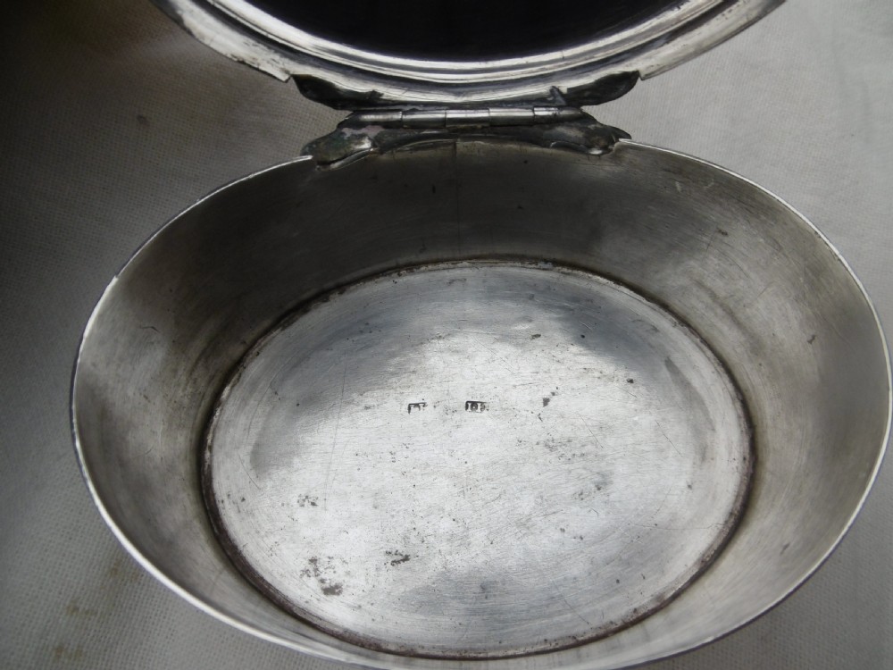 An 18th-century oval sterling silver box featuring a hinged lid engraved with a family crest depicting an arm holding a scimitar. View III