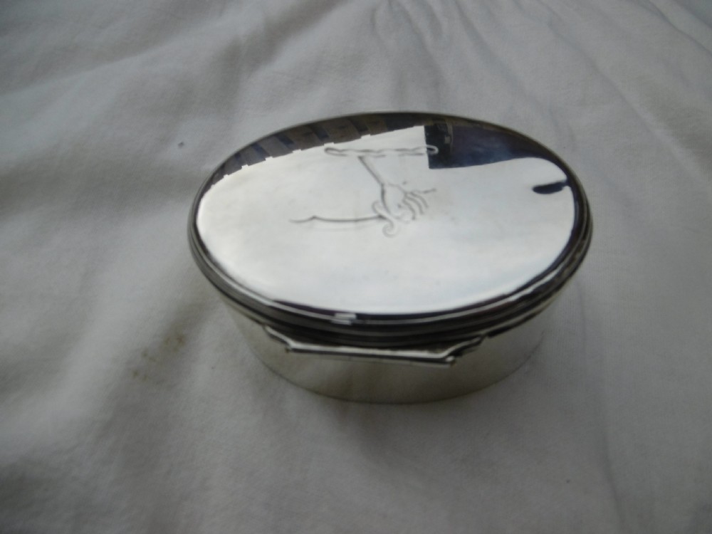 An 18th-century oval sterling silver box featuring a hinged lid engraved with a family crest depicting an arm holding a scimitar. View IV