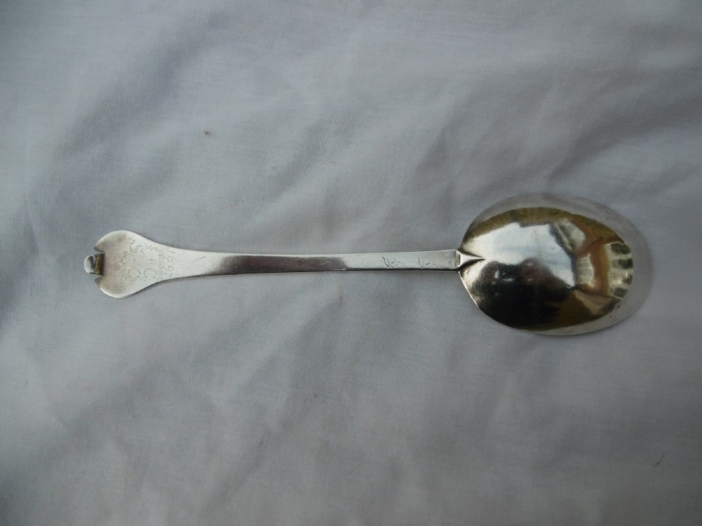 An antique silver trefid spoon featuring a notched three-lobed handle end with hand-engraved initials and an oval bowl.