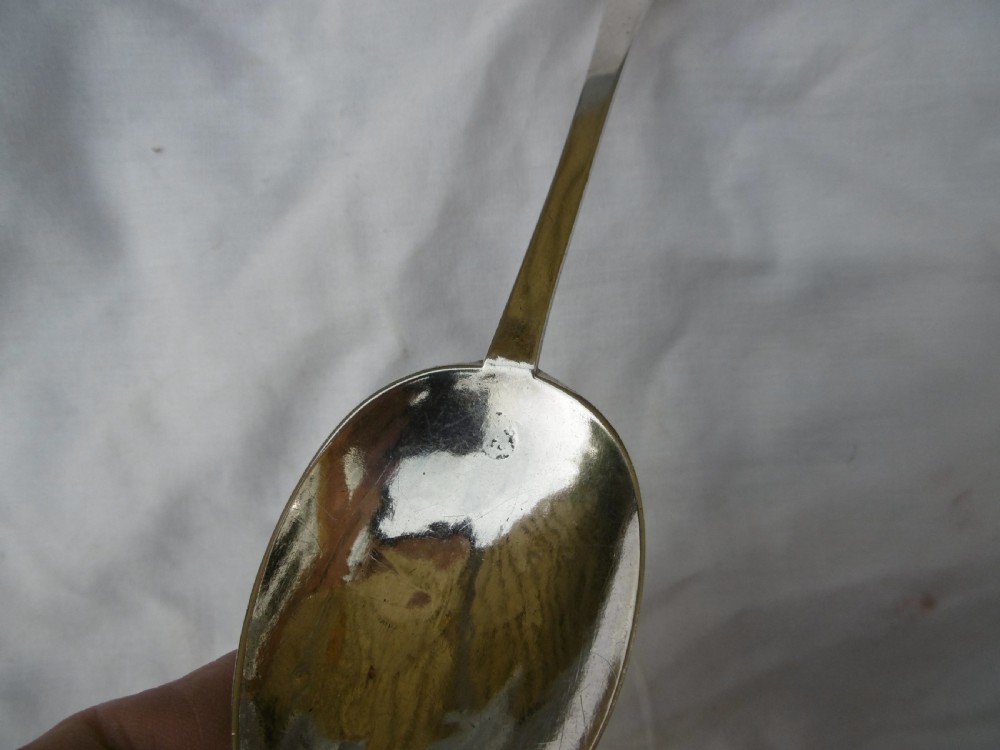 An antique silver trefid spoon featuring a notched three-lobed handle end with hand-engraved initials and an oval bowl. View V