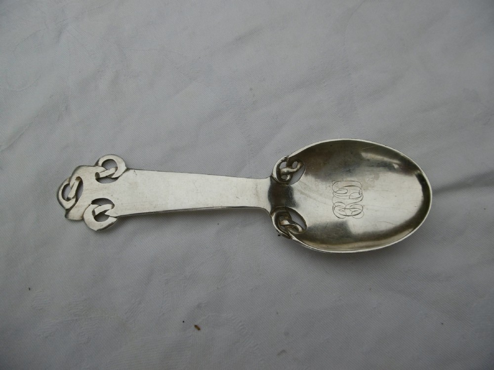 An Edwardian sterling silver spoon featuring stylised Celtic knotwork at the handle terminal and junction, with an engraved monogram inside the oval bowl.