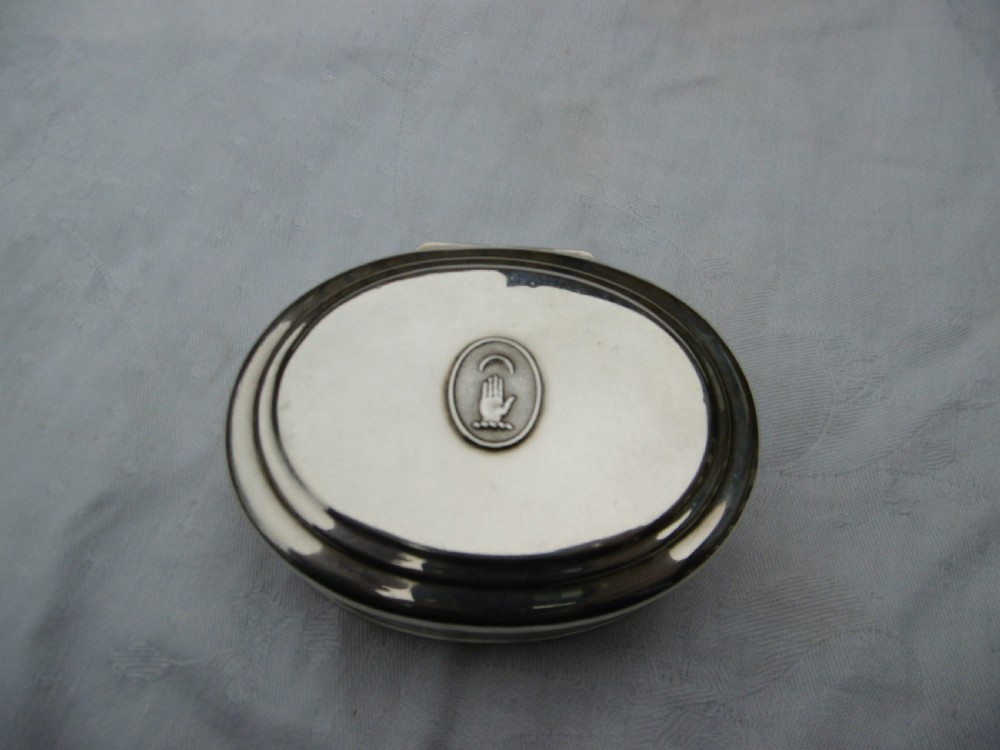 An oval 18th-century sterling silver tobacco box featuring a hinged lid engraved with a central oval crest depicting an open hand beneath a crescent moon.