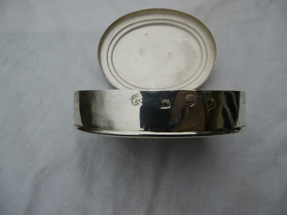 An oval 18th-century sterling silver tobacco box featuring a hinged lid engraved with a central oval crest depicting an open hand beneath a crescent moon. View III