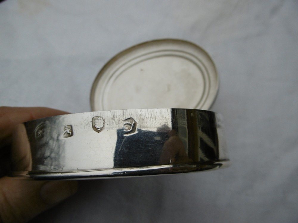An oval 18th-century sterling silver tobacco box featuring a hinged lid engraved with a central oval crest depicting an open hand beneath a crescent moon. View IV