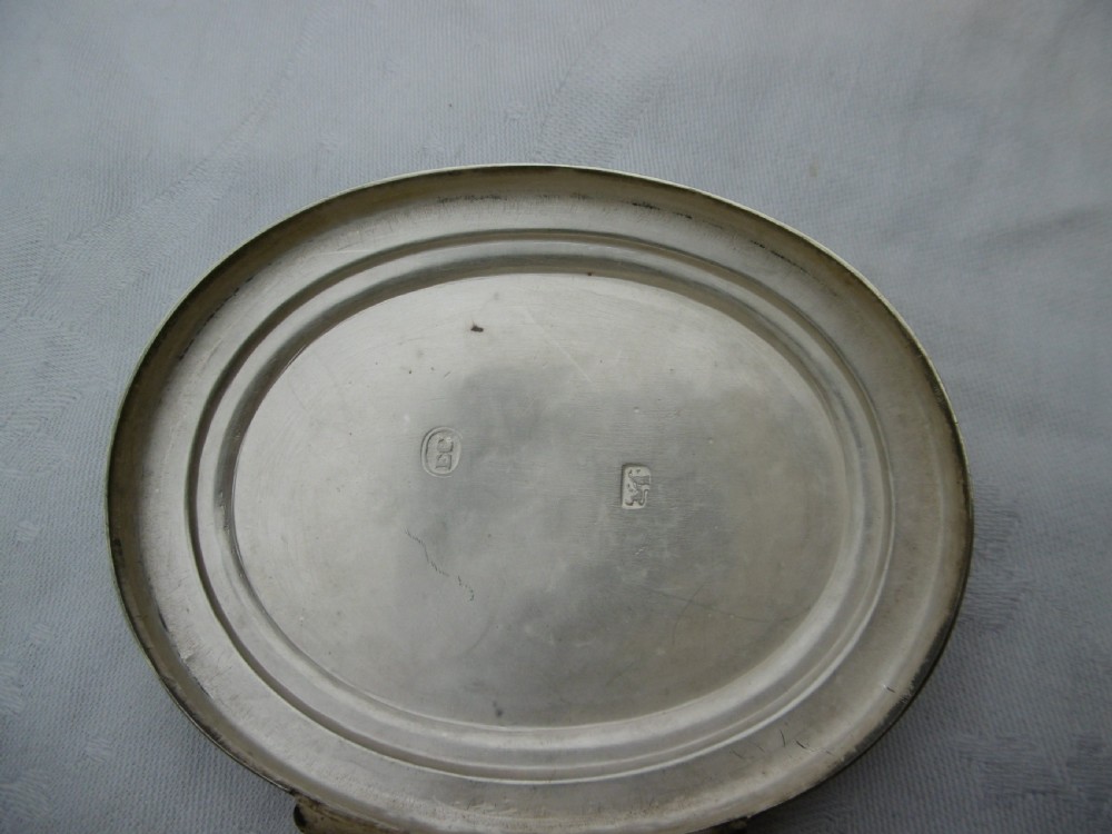 An oval 18th-century sterling silver tobacco box featuring a hinged lid engraved with a central oval crest depicting an open hand beneath a crescent moon. View V