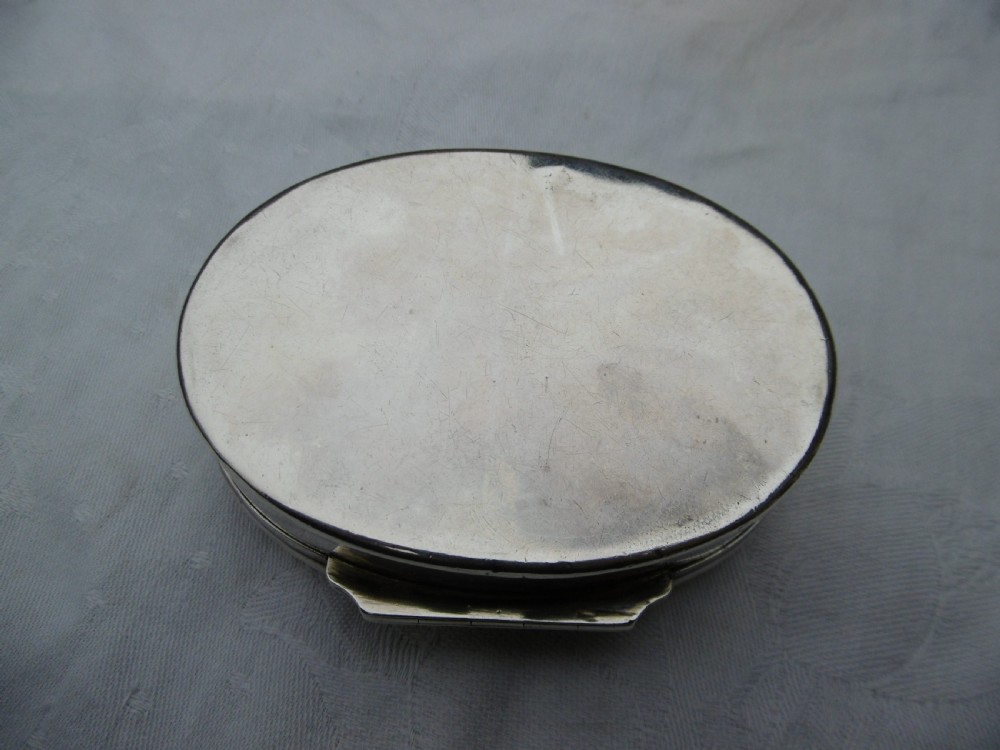 An oval 18th-century sterling silver tobacco box featuring a hinged lid engraved with a central oval crest depicting an open hand beneath a crescent moon. View VI