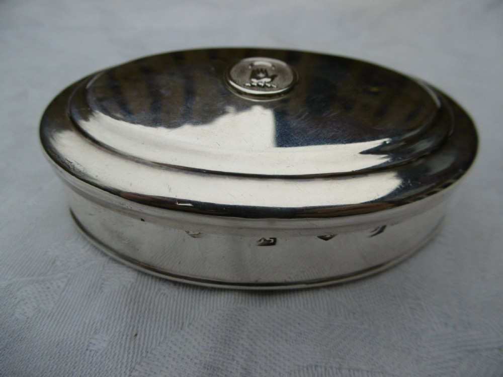 An oval 18th-century sterling silver tobacco box featuring a hinged lid engraved with a central oval crest depicting an open hand beneath a crescent moon. View VII