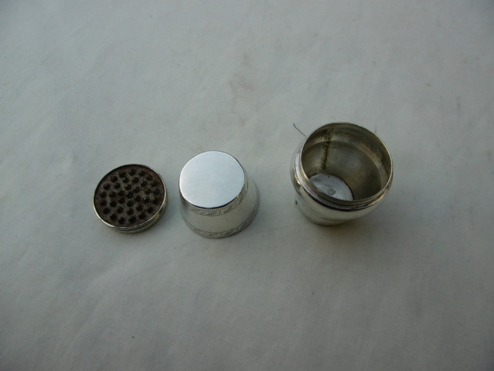 An antique Georgian sterling silver barrel-shaped nutmeg grater shown unscrewed into three component parts including cap, grater plate, and main body.