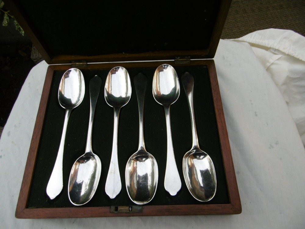 A set of six 1706 Queen Anne sterling silver dognose tablespoons arranged inside a velvet-lined wooden case.