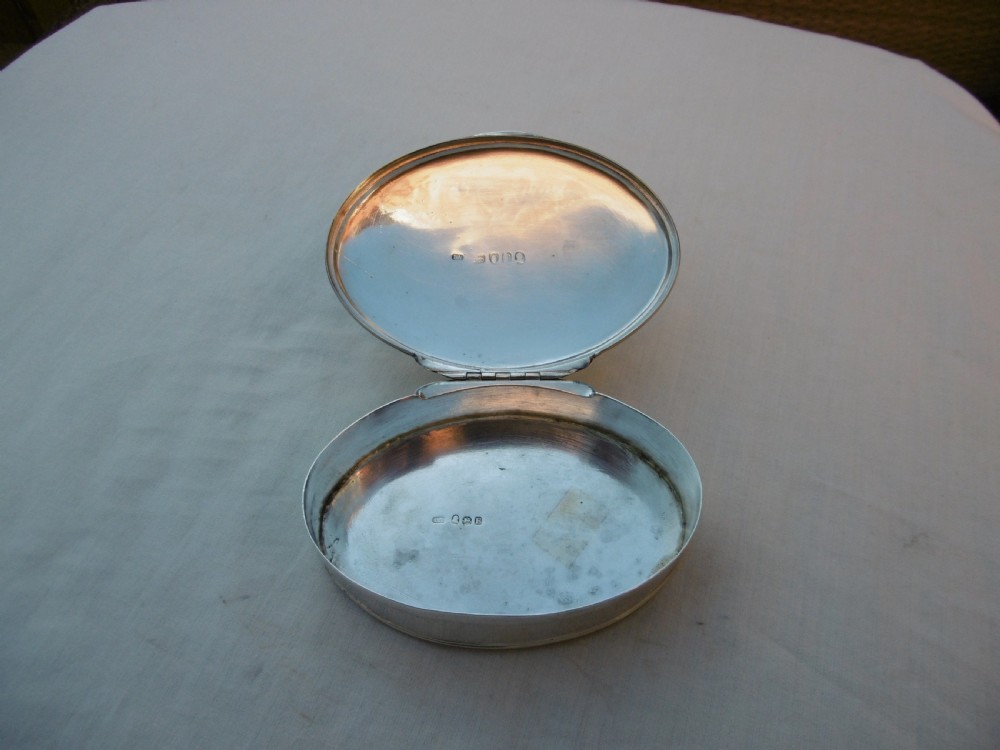 An open oval Georgian sterling silver tobacco box displaying stamped British hallmarks inside the lid and base.