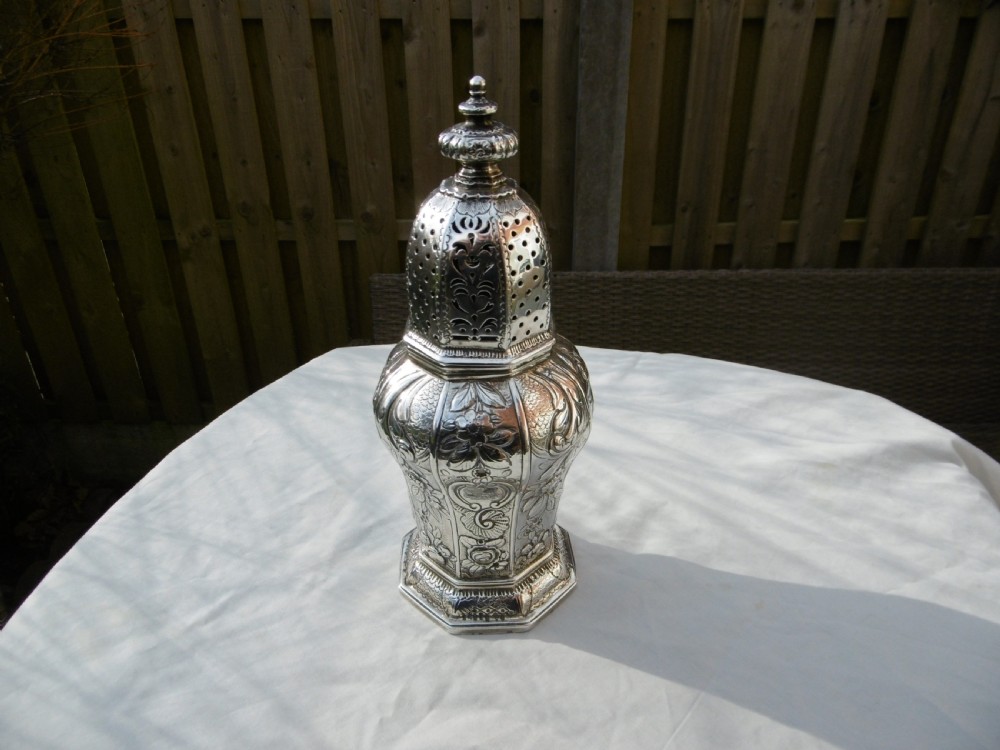 A Georgian sterling silver sugar castor featuring detailed floral chasing, a pierced dome lid, and a turned finial.