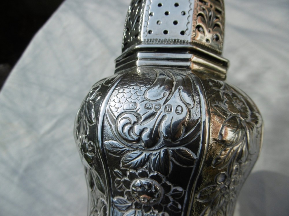A Georgian sterling silver sugar castor featuring detailed floral chasing, a pierced dome lid, and a turned finial. View II