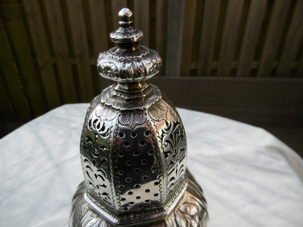 A Georgian sterling silver sugar castor featuring detailed floral chasing, a pierced dome lid, and a turned finial. View IV