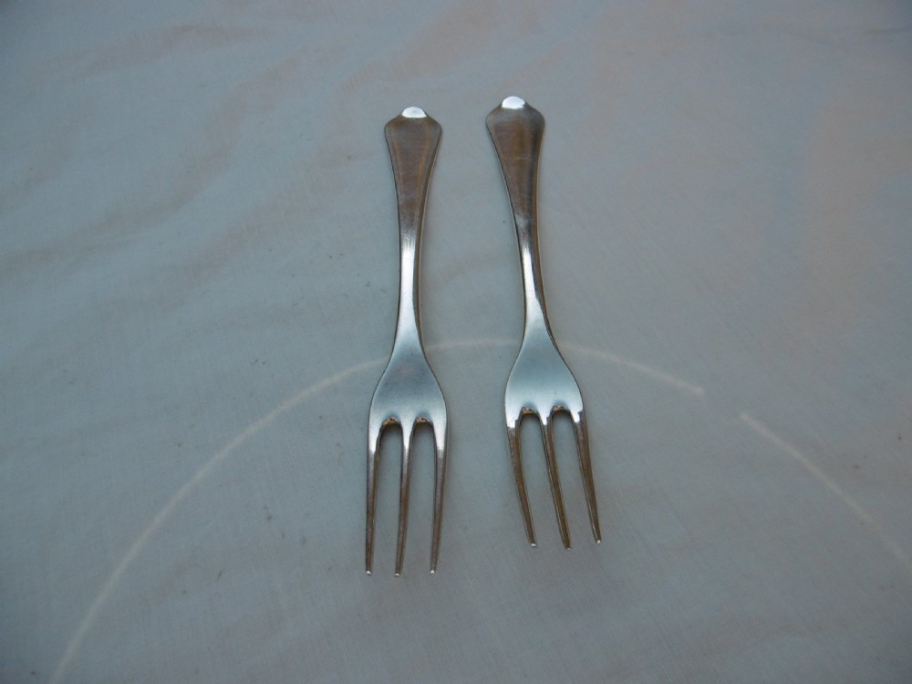 A pair of antique silver table forks featuring three tines and dognose handles engraved with armorial crests. View IV