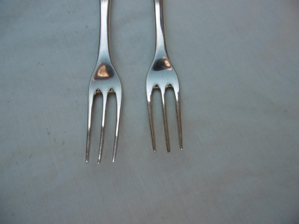A pair of antique silver table forks featuring three tines and dognose handles engraved with armorial crests. View V