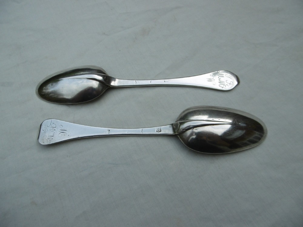 A pair of 1706 Scottish Queen Anne sterling silver dognose tablespoons featuring rat-tail bowl supports and engraved initials on the handle terminals.