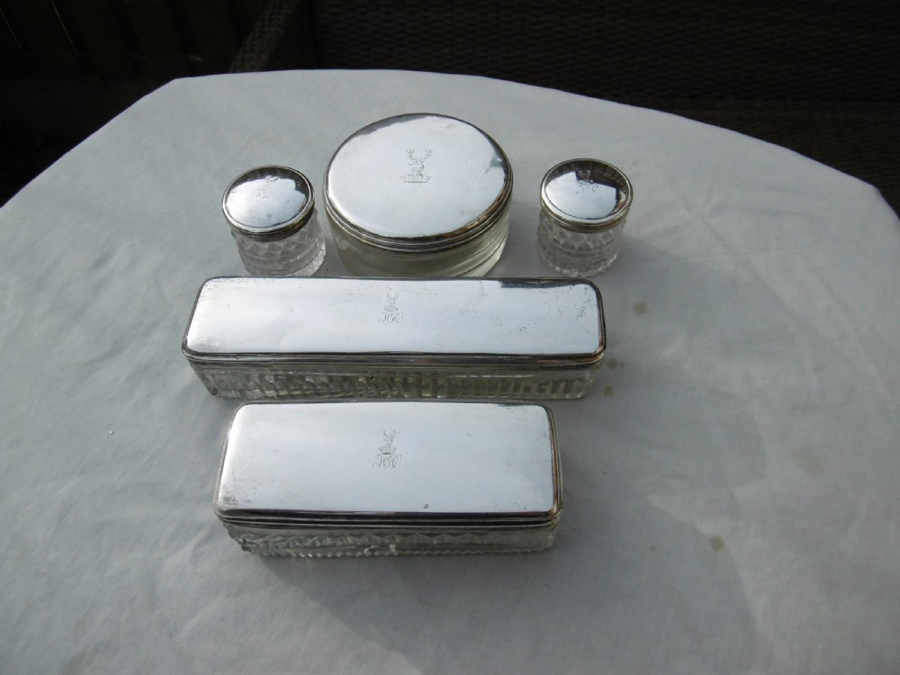 A five-piece Georgian sterling silver and cut glass dressing table set featuring engraved stag crests on silver lids.