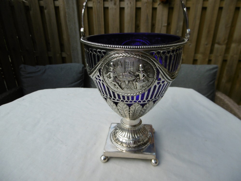 An 18th-century Adam style silver swing-handled basket with a cobalt blue glass liner, resting on a pedestal and square base with ball feet. View II