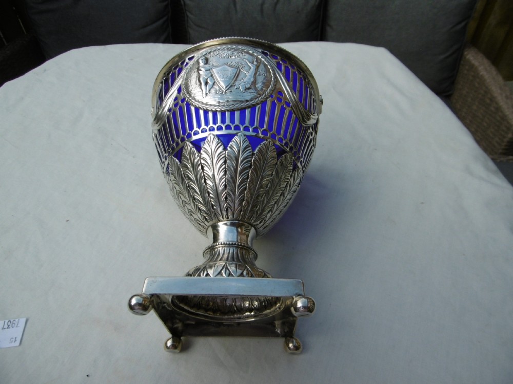 An 18th-century Adam style silver swing-handled basket with a cobalt blue glass liner, resting on a pedestal and square base with ball feet. View III