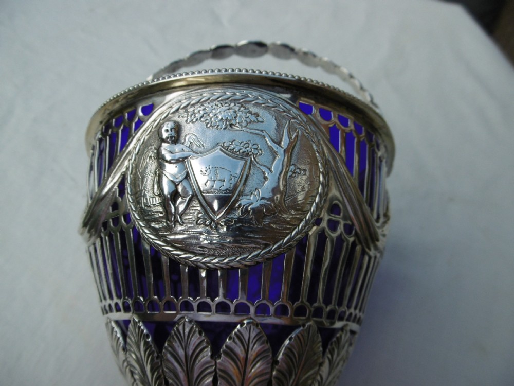 An 18th-century Adam style silver swing-handled basket with a cobalt blue glass liner, resting on a pedestal and square base with ball feet. View IV