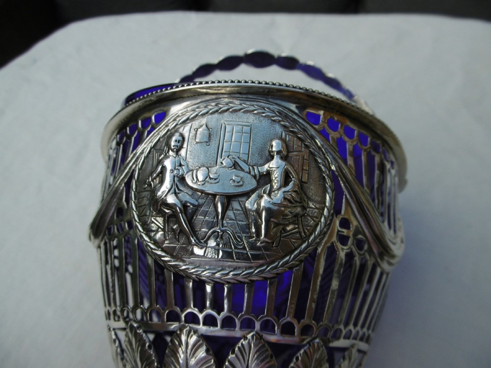 An 18th-century Adam style silver swing-handled basket with a cobalt blue glass liner, resting on a pedestal and square base with ball feet. View V
