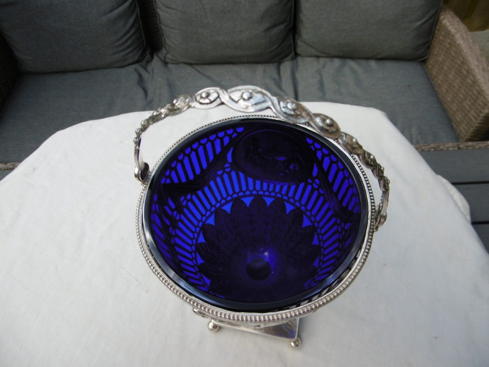An 18th-century Adam style silver swing-handled basket with a cobalt blue glass liner, resting on a pedestal and square base with ball feet. View VII