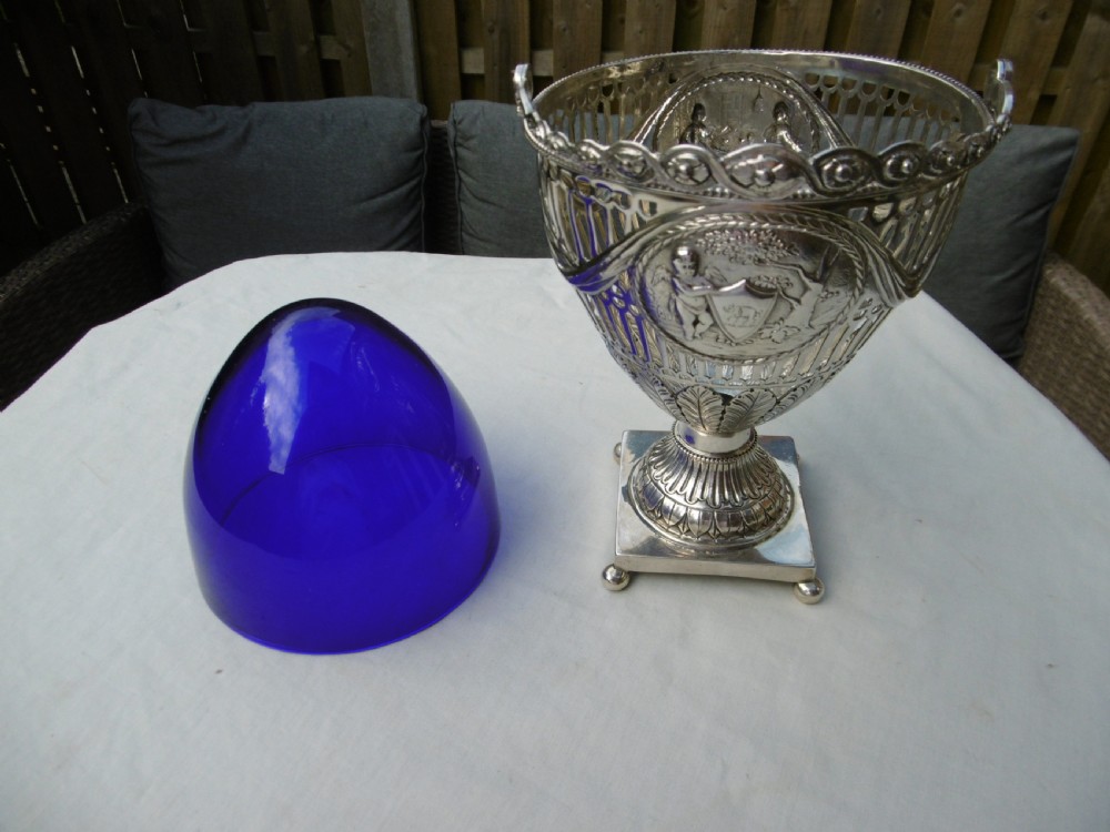 An 18th-century Adam style silver swing-handled basket with a cobalt blue glass liner, resting on a pedestal and square base with ball feet. View VIII