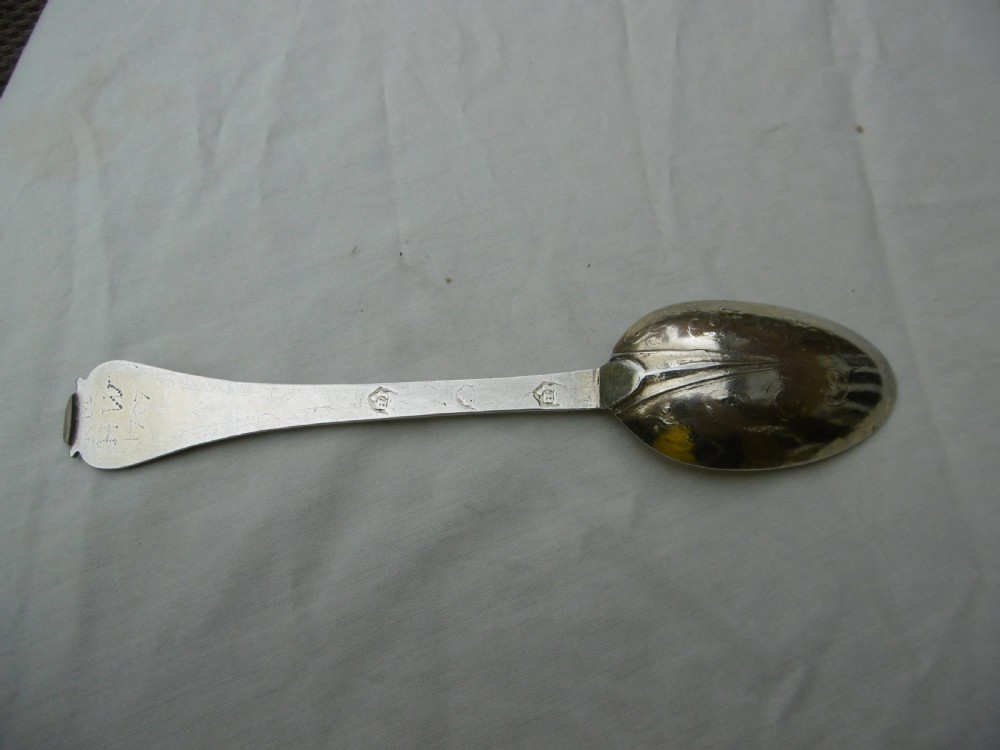 Reverse view of a silver tablespoon dated 1707 with a lace-back pattern and hallmarks along the handle.