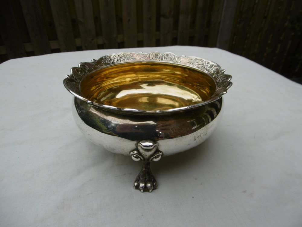 A George II sterling silver bowl featuring a scalloped chased rim, a gilded interior wash, and supported on three cast feet.