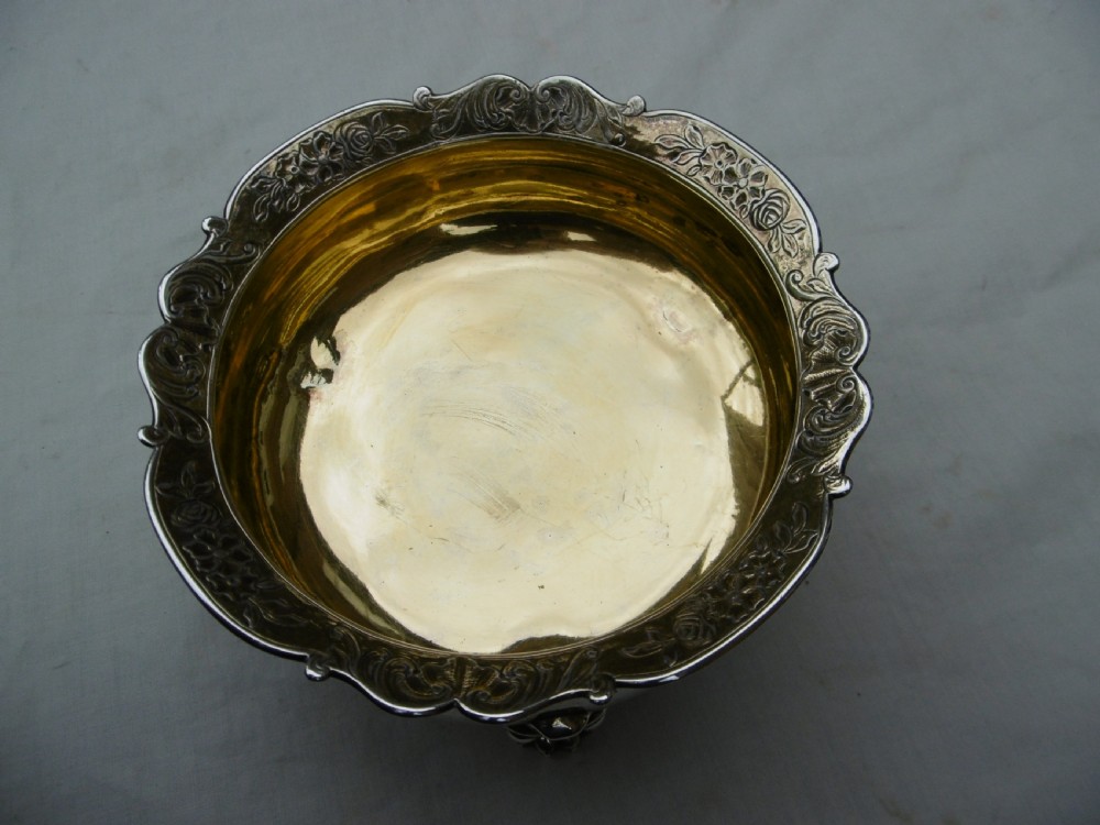 A George II sterling silver bowl featuring a scalloped chased rim, a gilded interior wash, and supported on three cast feet. View III