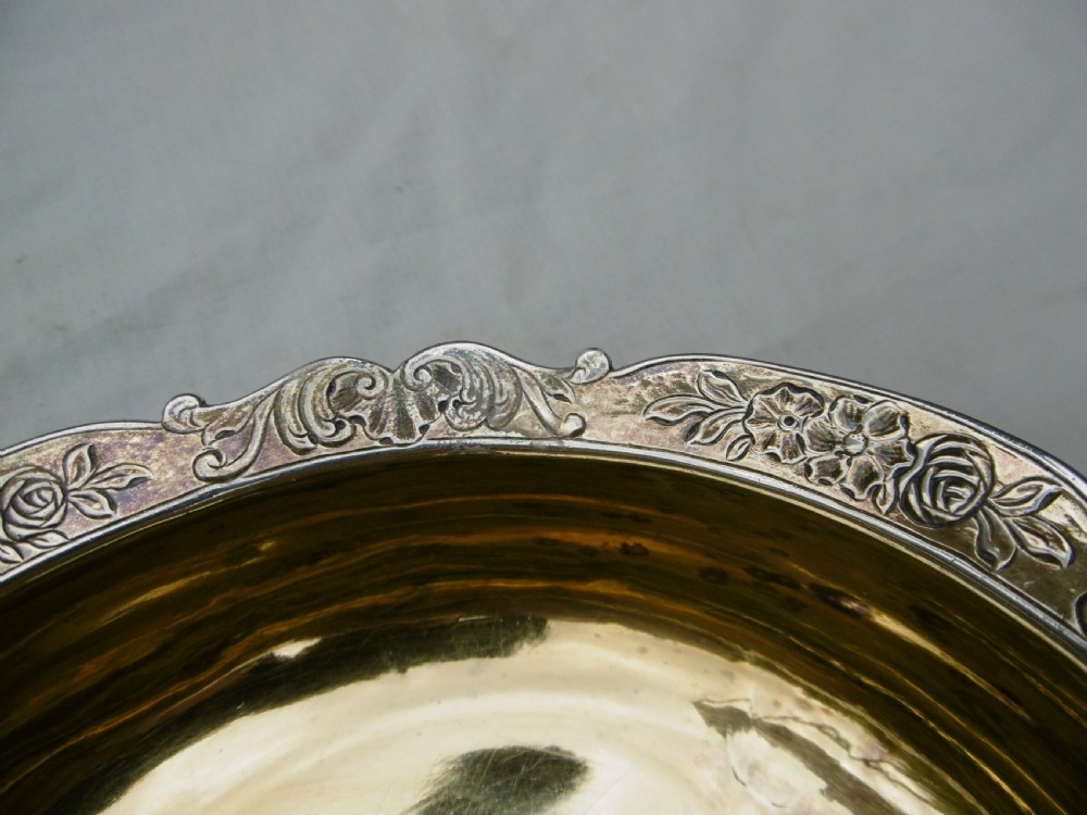 A George II sterling silver bowl featuring a scalloped chased rim, a gilded interior wash, and supported on three cast feet. View IV