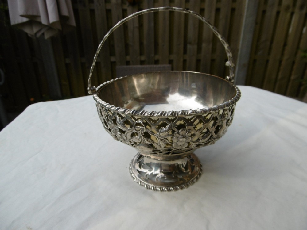 An 18th-century Irish Georgian sterling silver basket featuring pierced lattice work, floral motifs, a pedestal base, and an arched swing handle.