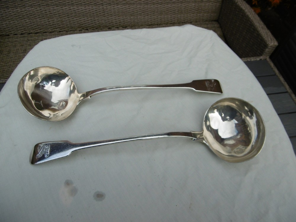 A pair of Georgian sterling silver soup ladles featuring Fiddle pattern handles engraved with crests and deep round silver bowls.