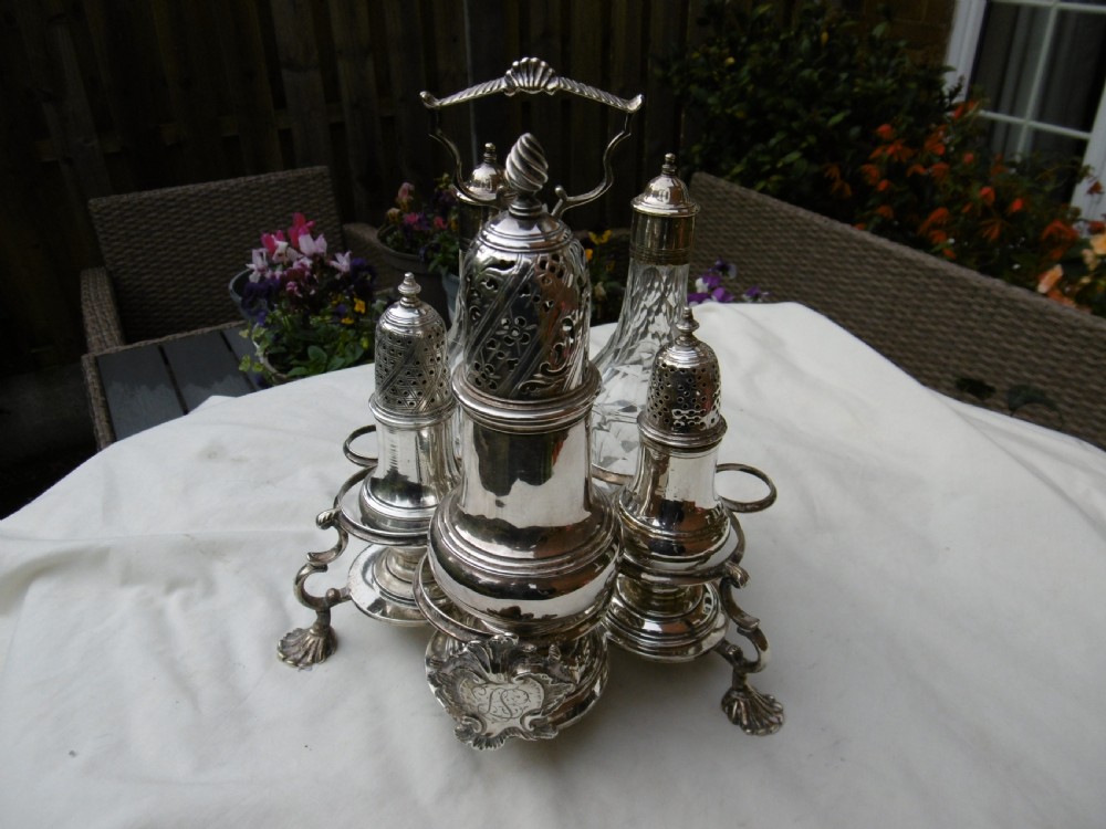 An 18th-century Georgian sterling silver Warwick cruet frame holding silver casters and cut glass bottles set upon shell-form feet.