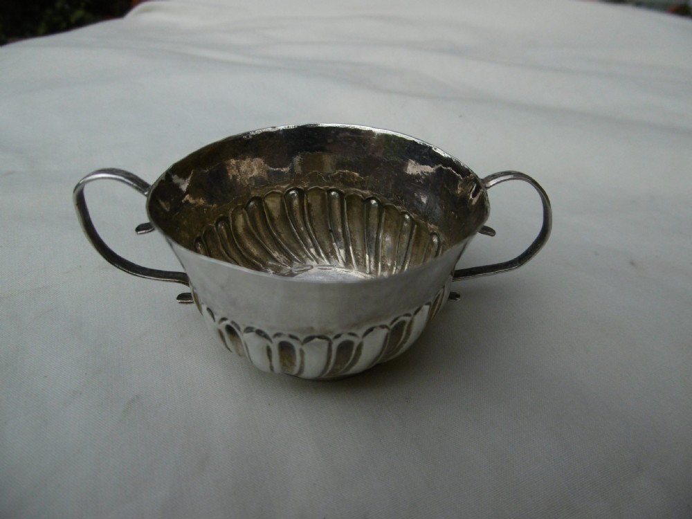 A small late 17th-century silver porringer featuring two wire handles and spiral fluted embossing around the lower half of the bowl.