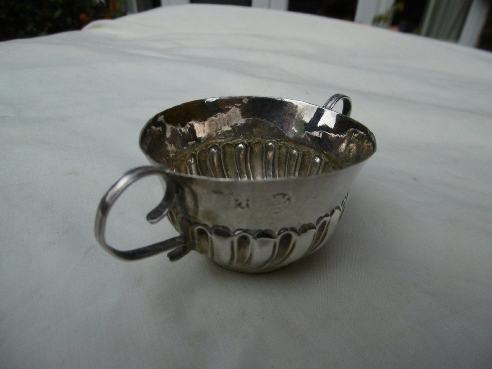 A small late 17th-century silver porringer featuring two wire handles and spiral fluted embossing around the lower half of the bowl. View II