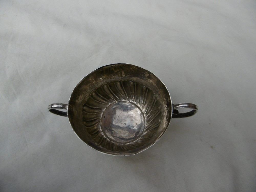 A small late 17th-century silver porringer featuring two wire handles and spiral fluted embossing around the lower half of the bowl. View V